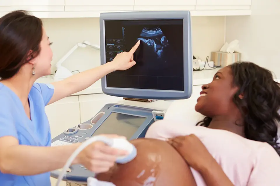 Sonographer pointing to an ultrasound image on screen while a smiling pregnant patient looks on